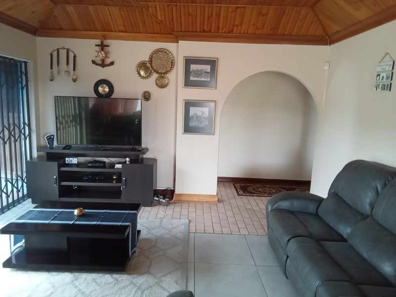 A living room featuring a timber tongue and groove ceiling, tiled flooring, and a decorative archway leading to an adjacent space.