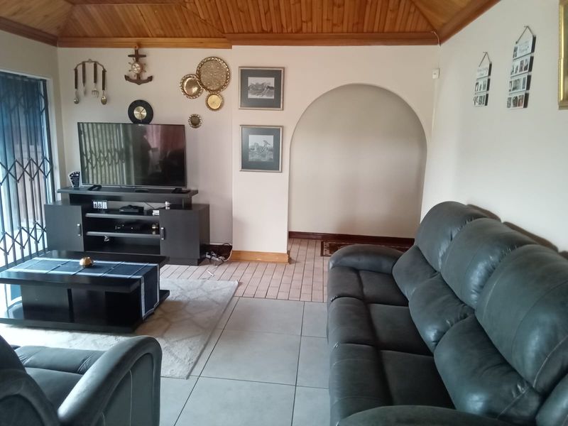 A living room featuring a timber tongue and groove ceiling, tiled flooring, and a decorative archway leading to an adjacent space.