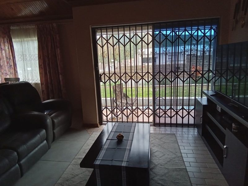 A living room featuring tiled flooring, a timber ceiling, and a sliding glass door with a security gate leading to the outdoor area.