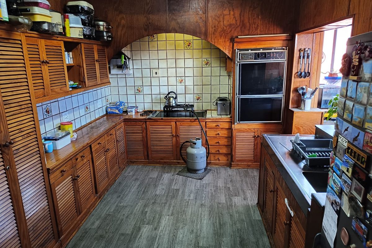 A traditional kitchen featuring extensive wooden cabinetry, a double wall oven, gas cooktop, and tiled backsplash with a neutral laminate floor.