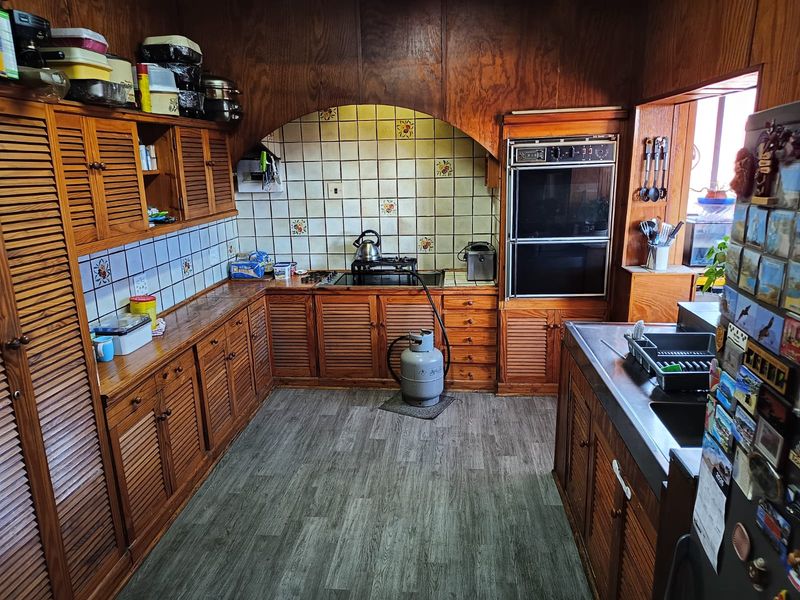 A traditional kitchen featuring extensive wooden cabinetry, a double wall oven, gas cooktop, and tiled backsplash with a neutral laminate floor.