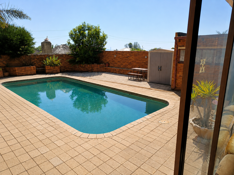 Outdoor pool area featuring a paved deck, brick boundary walls, and raised planters, viewed from an adjacent interior space.