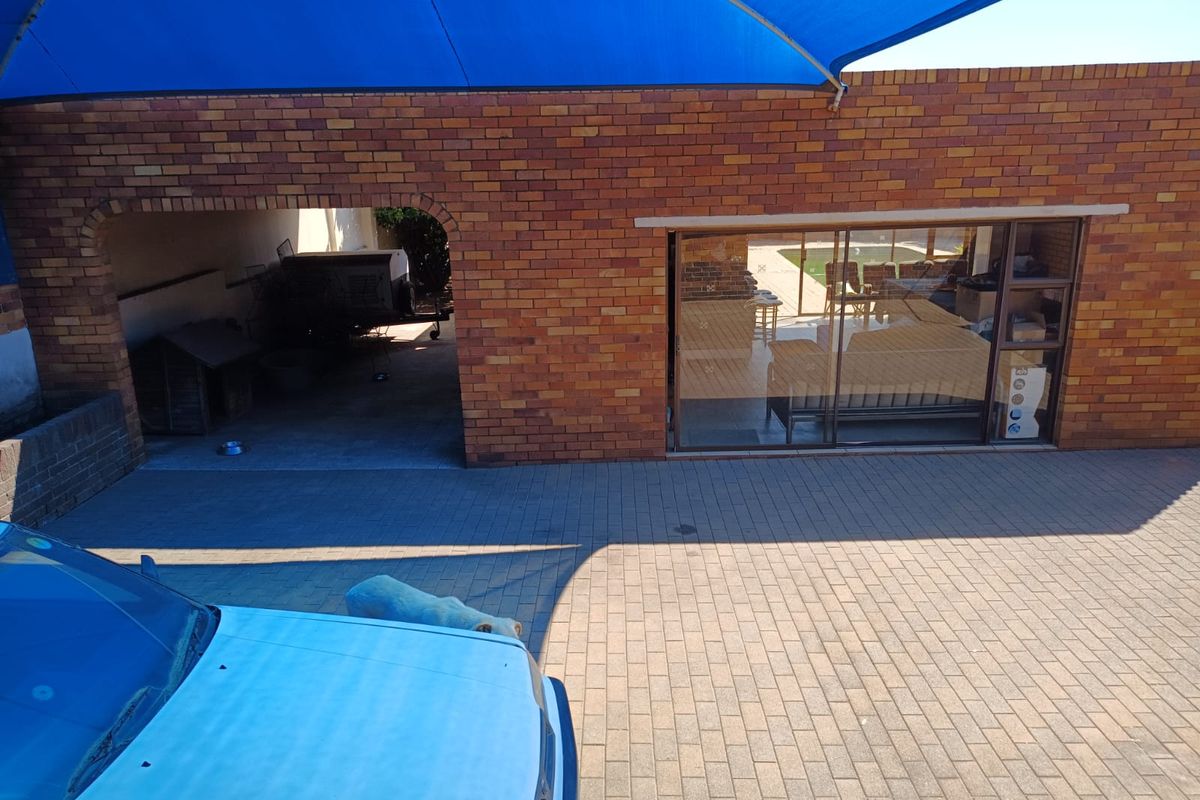 Rear exterior view featuring a brick facade, paved driveway, covered carport area, and a large sliding glass door leading into the home.