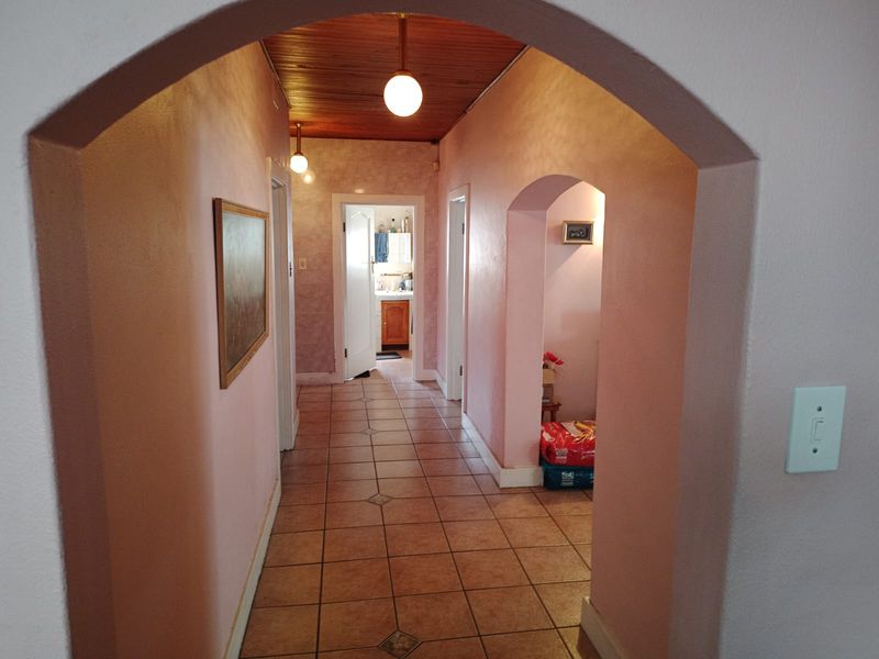 A spacious hallway featuring ceramic tile flooring, arched architectural details, and a timber-clad ceiling, providing access to adjacent rooms.