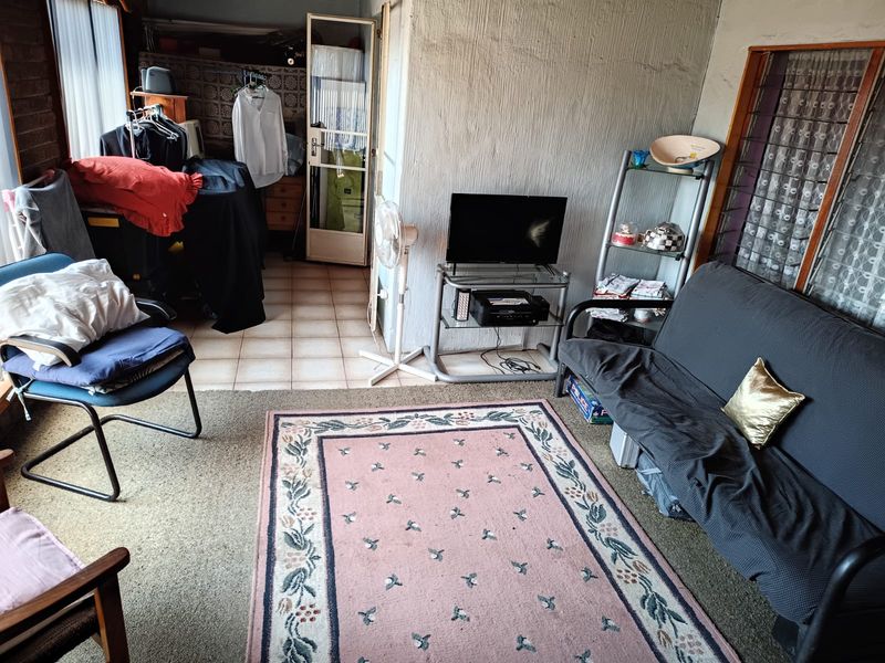 A living area featuring a mix of tiled and carpeted flooring with textured walls and louvre windows, currently used as a multi-purpose living space.