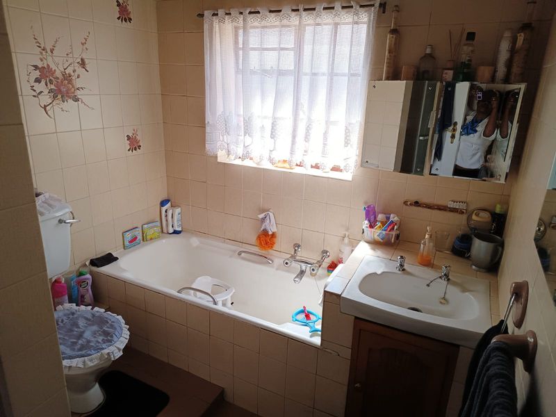 A functional bathroom featuring a bathtub, vanity basin, and toilet with dated wall tiling and cabinetry, offering potential for a modern renovation.