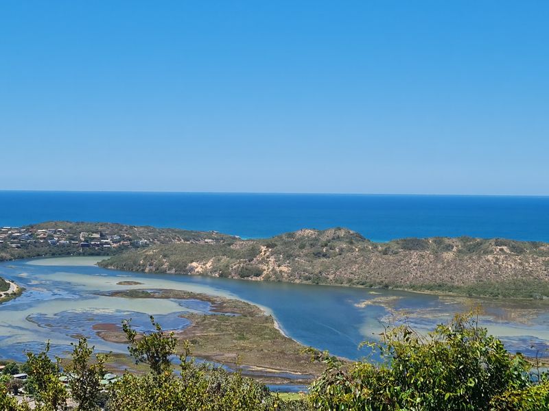 A scenic elevated view overlooking a coastal lagoon, natural dunes, and the distant ocean horizon.