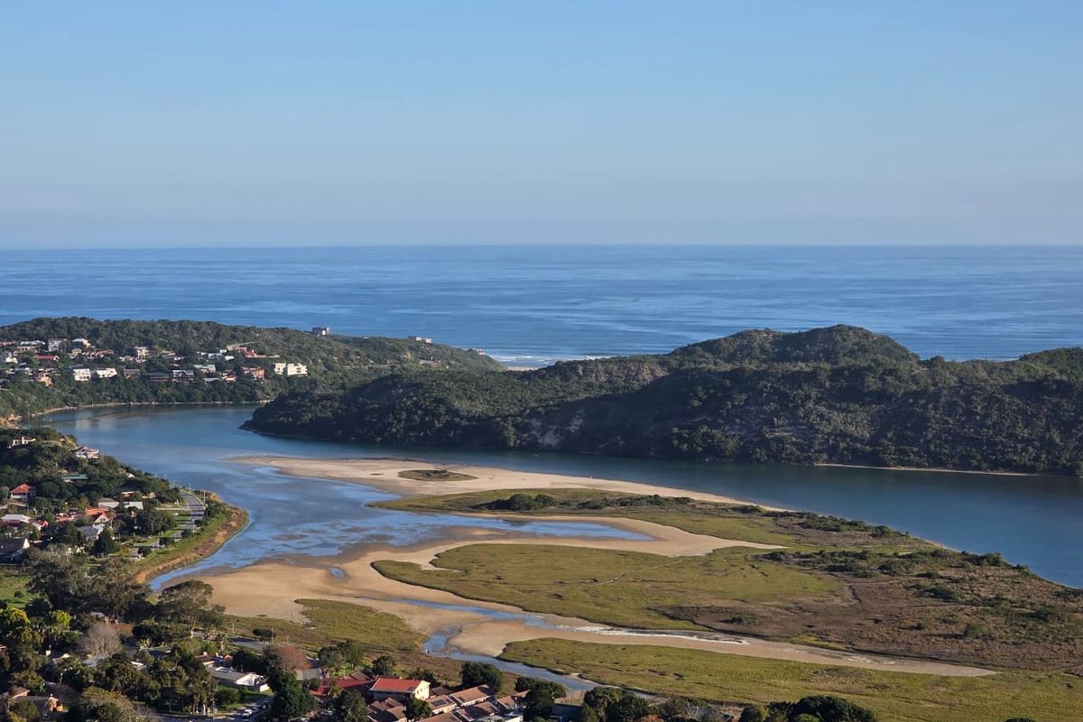 An elevated aerial view showcasing the coastal estuary, surrounding natural landscape, and nearby residential neighborhood.