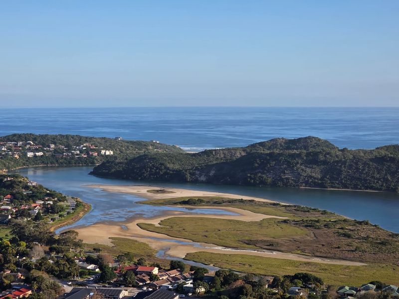 An elevated aerial view showcasing the coastal estuary, surrounding natural landscape, and nearby residential neighborhood.