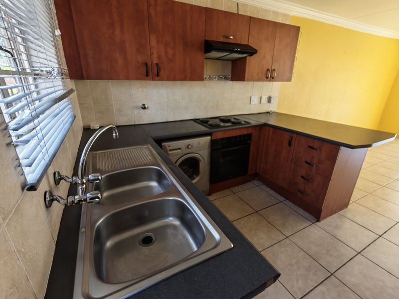 A functional kitchen featuring wooden cabinetry, laminate countertops, a double bowl sink, and built-in cooking appliances with tiled flooring and splashbacks.