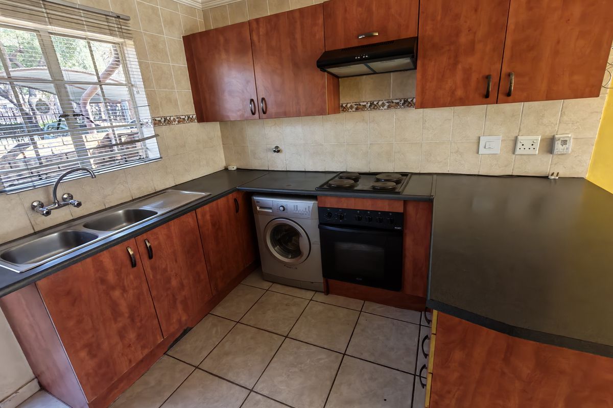 A functional kitchen featuring laminate cabinetry, dark countertops, a built-in oven with hob, and tiled finishes throughout.