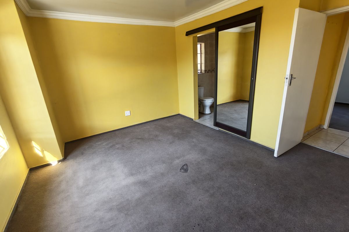 An empty bedroom featuring yellow walls, carpet flooring, and a built-in sliding door wardrobe with direct access to an en-suite bathroom.
