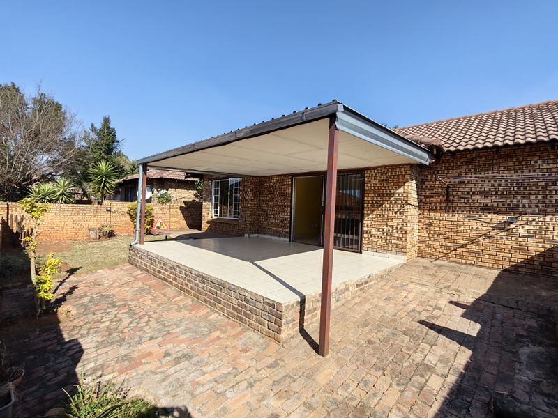 A covered outdoor patio area with tiled flooring, brick facade, and direct access to the interior, overlooking a paved courtyard and garden space.