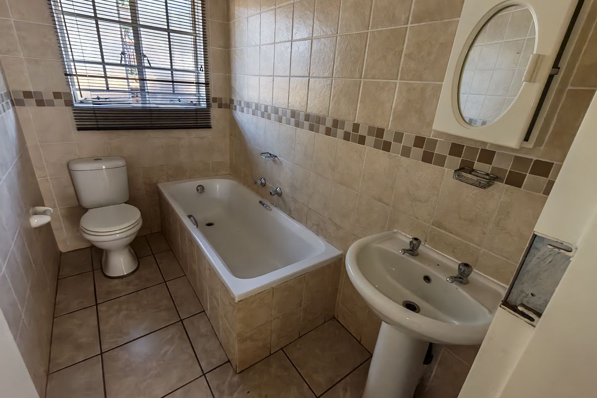 A functional bathroom featuring a bathtub, pedestal basin, and toilet with neutral tiled finishes, offering a clean canvas for potential modern updates.