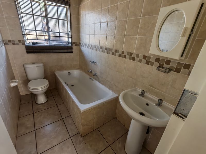 A functional bathroom featuring a bathtub, pedestal basin, and toilet with neutral tiled finishes, offering a clean canvas for potential modern updates.