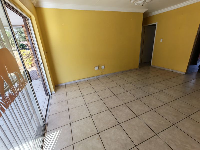 An empty living room featuring ceramic floor tiles, yellow painted walls, and a sliding glass door providing access to the outdoor area.