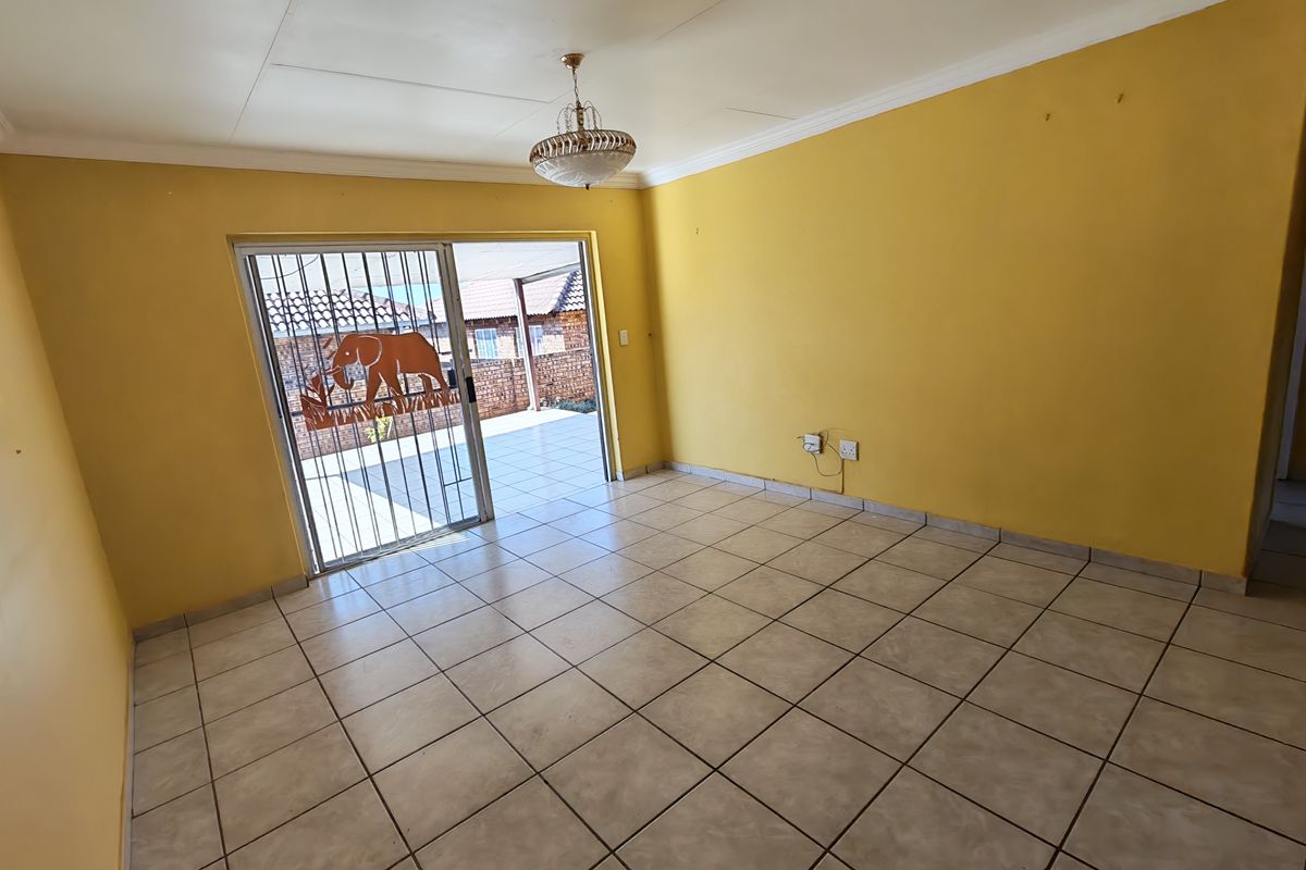 An empty living room featuring tiled flooring, a sliding glass door with a security gate, and access to an outdoor patio area.