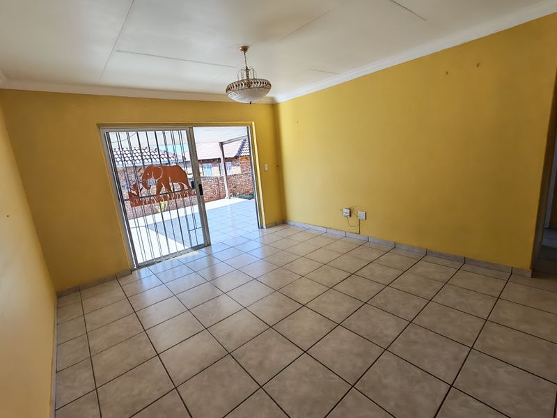 An empty living room featuring tiled flooring, a sliding glass door with a security gate, and access to an outdoor patio area.