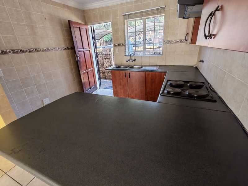 A functional kitchen featuring dark laminate countertops, built-in cabinetry, an electric hob, and a double sink with direct access to the exterior.
