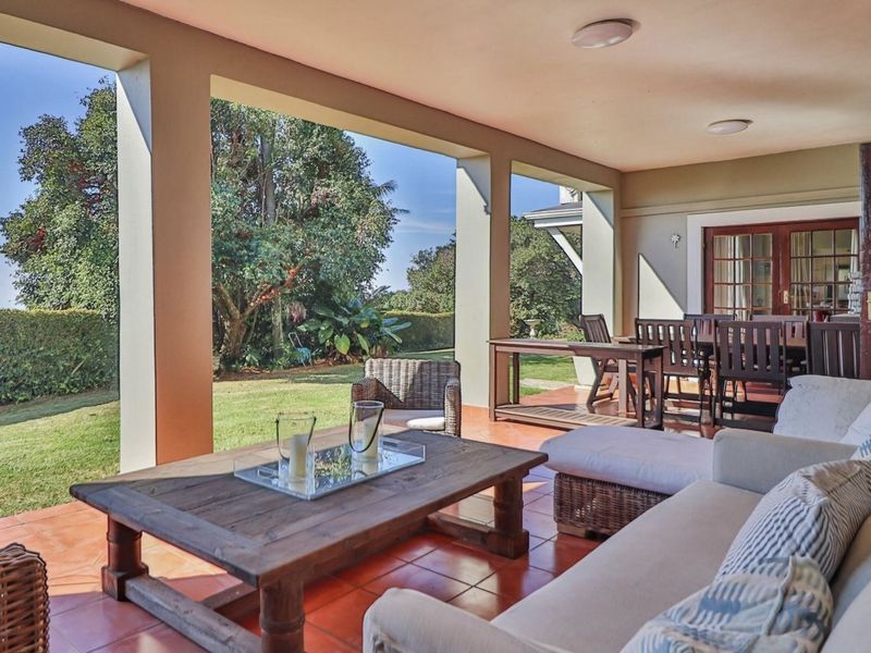 A spacious covered patio featuring terracotta tiling and support columns, offering a seamless transition to the garden area.