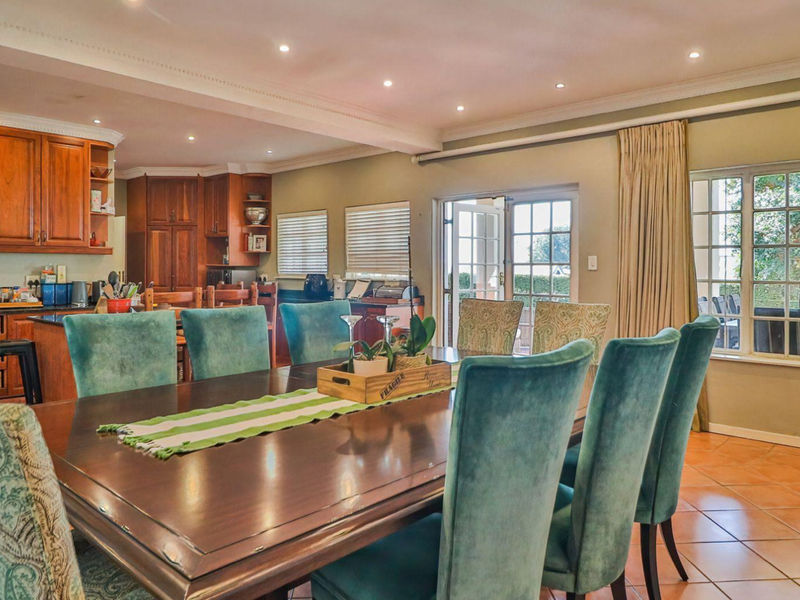 Spacious open-plan dining and kitchen area featuring warm wooden cabinetry, granite countertops, terracotta flooring, and direct access to the outdoor patio through french doors.