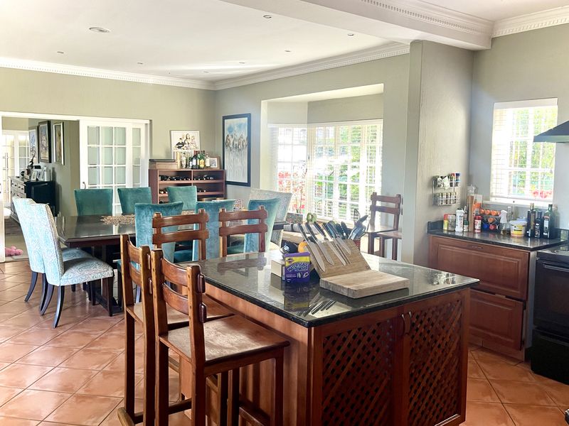 Spacious open-plan kitchen and dining area featuring a central island, granite countertops, tiled flooring, and classic french doors leading to adjacent rooms.