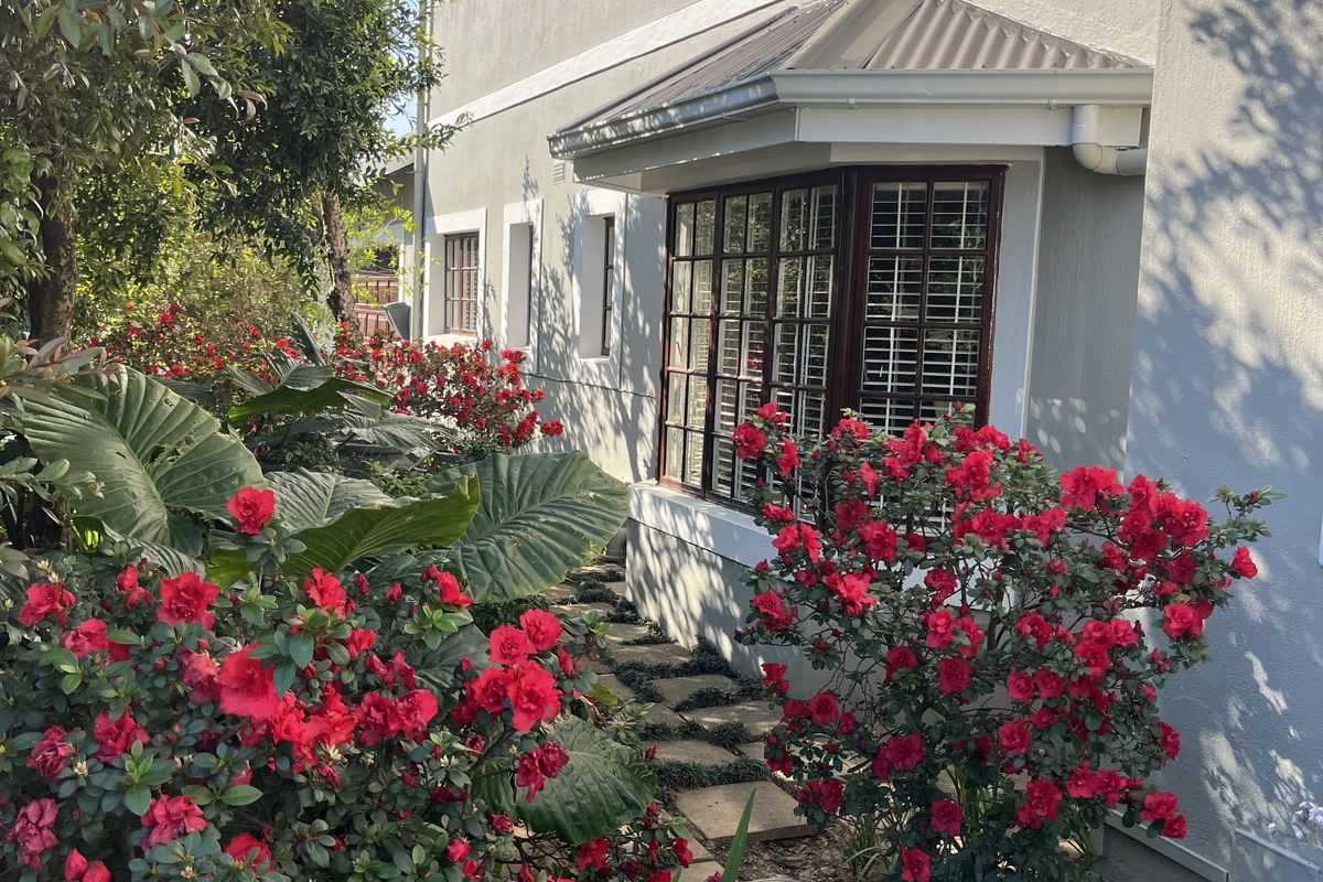 A well-maintained rear exterior view of the townhouse featuring a bay window, metal awning, and a stone pathway surrounded by lush garden landscaping.
