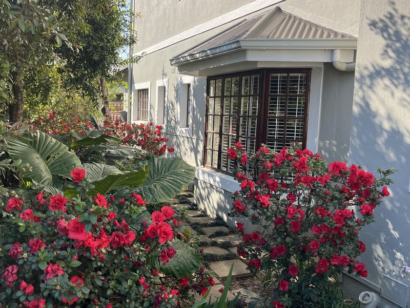 A well-maintained rear exterior view of the townhouse featuring a bay window, metal awning, and a stone pathway surrounded by lush garden landscaping.