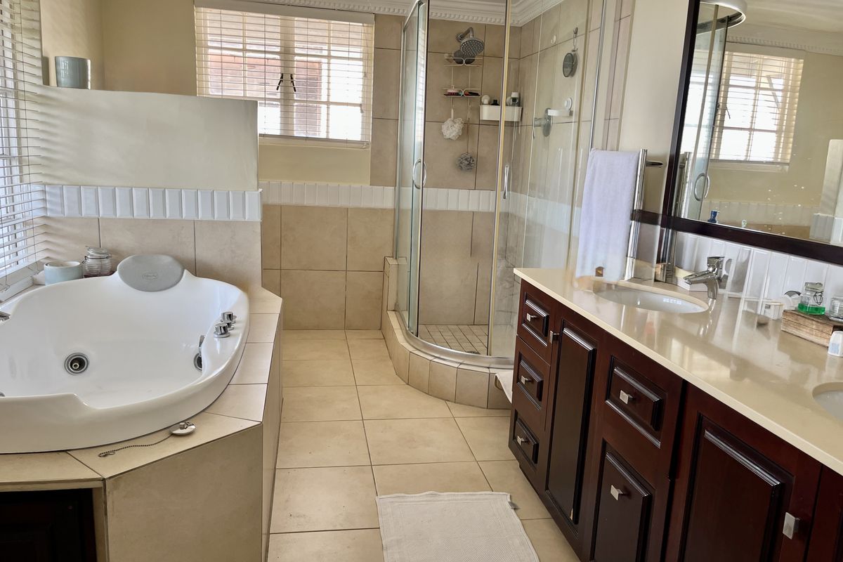 Spacious bathroom featuring a corner spa bath, a separate curved glass shower, and a double vanity with dark wood cabinetry and stone countertops.