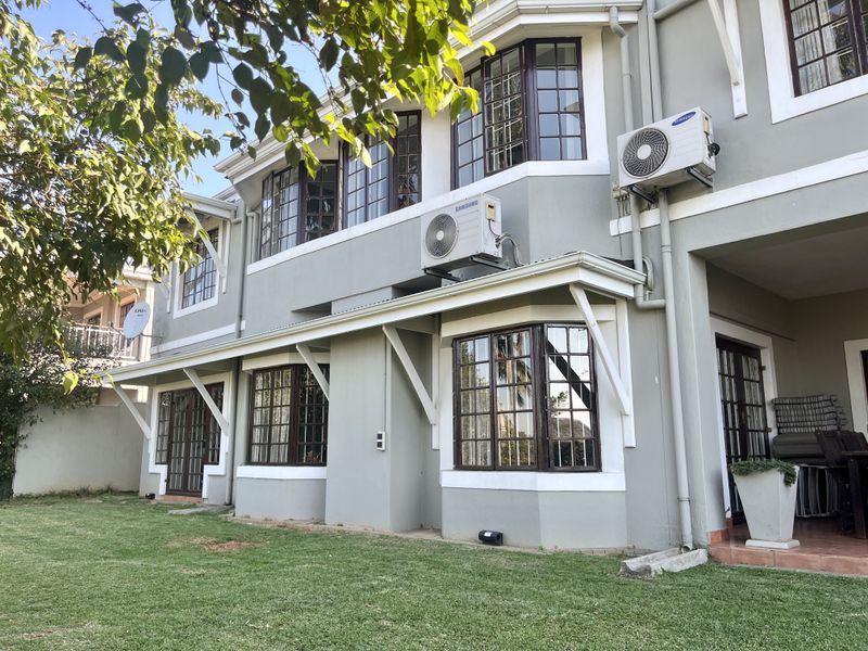 Rear view of a two-story townhouse featuring bay windows, exterior air conditioning units, and a paved patio area overlooking a private garden.
