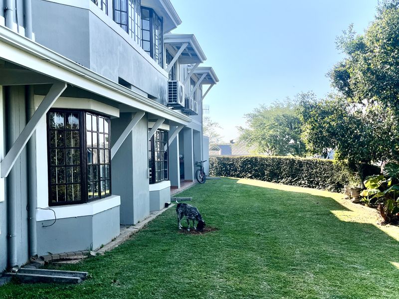 Rear view of the townhouse featuring a well-maintained lawn, mature hedging, and multiple bay windows with dark frames.