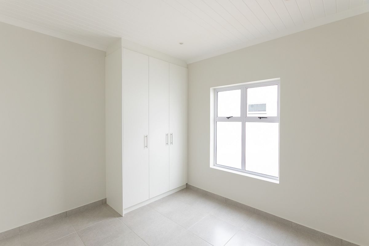 A bright, empty bedroom featuring neutral tiled flooring, a built-in white wardrobe, and a clean tongue and groove ceiling finish.