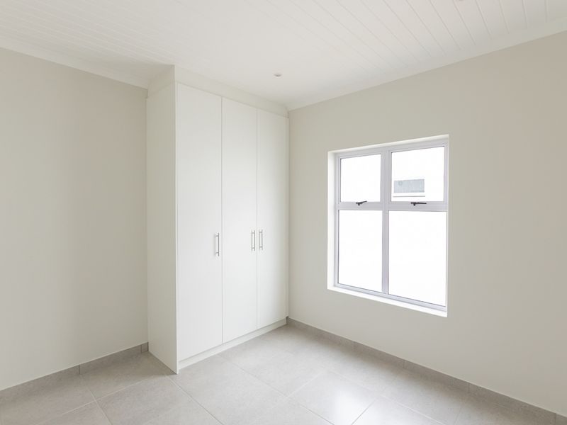 A bright, empty bedroom featuring neutral tiled flooring, a built-in white wardrobe, and a clean tongue and groove ceiling finish.