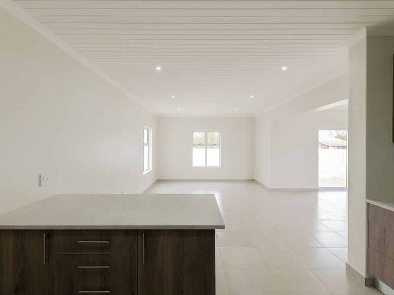 Spacious open-plan living and kitchen area featuring modern cabinetry, neutral tiled flooring, and recessed lighting in a clean, bright, and vacant interior space.