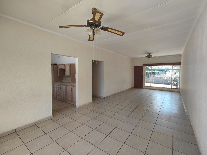 Spacious open-plan living area featuring neutral ceramic floor tiles, ceiling fans, and direct access to the kitchen and outdoor space.