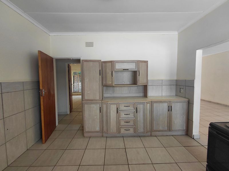 A functional kitchen area featuring built-in cabinetry, tiled flooring, and a tiled splashback, presenting a clean and empty space ready for updates.