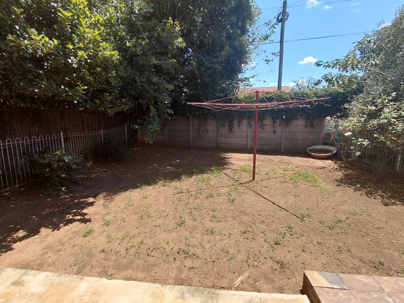 A private rear garden area featuring a precast concrete boundary wall, metal fencing, and a rotary clothesline, with potential for landscaping improvements.