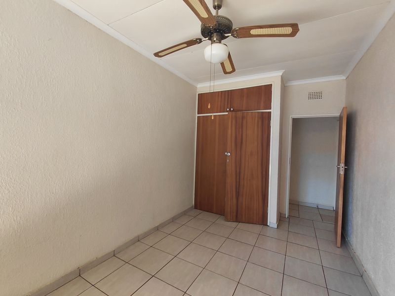 An empty bedroom featuring tiled flooring, built-in wooden cupboards, and a ceiling fan, offering a neutral canvas for personalization.