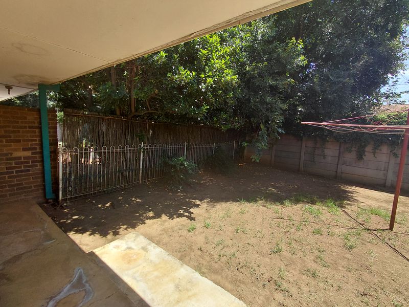 A covered patio area overlooking a private rear garden with established trees, brick walling, and perimeter fencing.