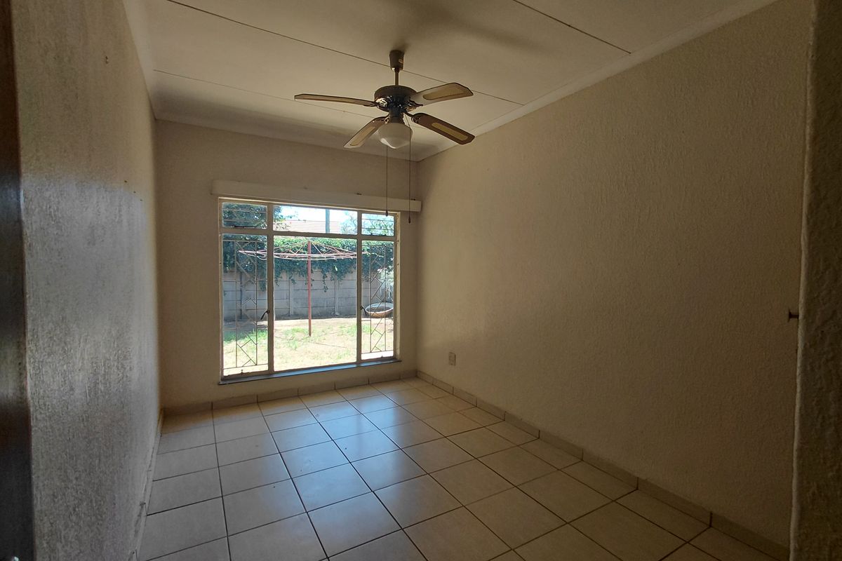 An empty bedroom featuring tiled flooring, a ceiling fan, and a large window with security bars overlooking the rear garden.