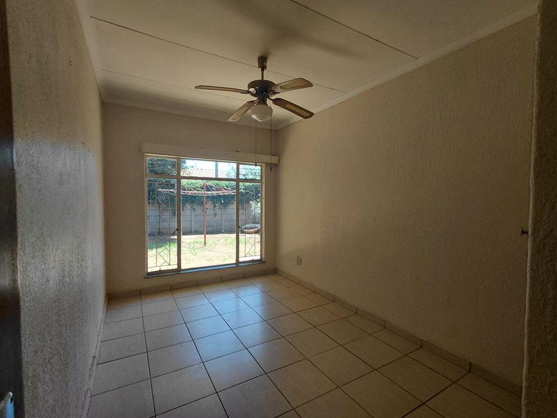 An empty bedroom featuring tiled flooring, a ceiling fan, and a large window with security bars overlooking the rear garden.