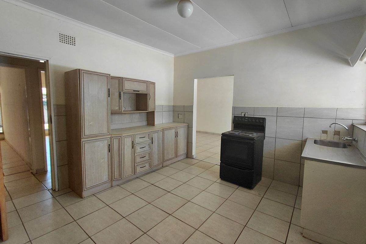A functional kitchen featuring tiled flooring, built-in cabinetry, a stainless steel sink, and a freestanding stove, offering a blank canvas for renovation.