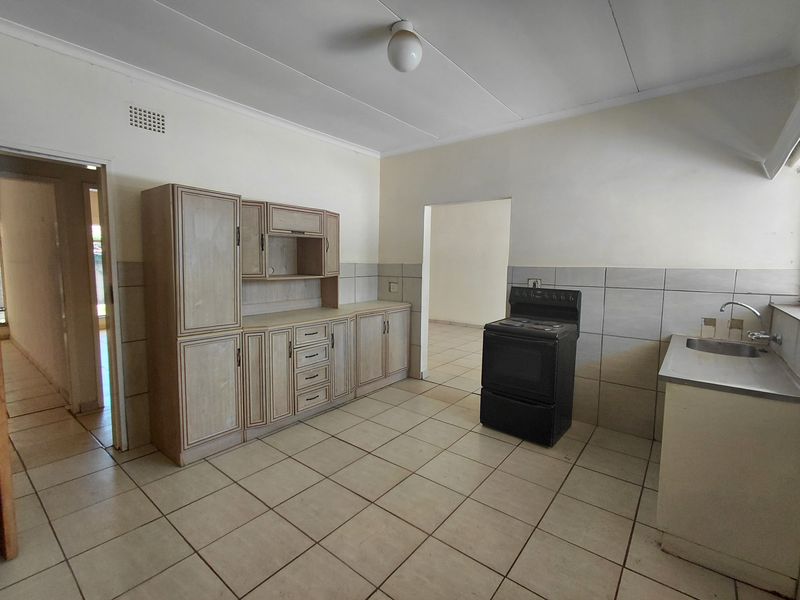 A functional kitchen featuring tiled flooring, built-in cabinetry, a stainless steel sink, and a freestanding stove, offering a blank canvas for renovation.
