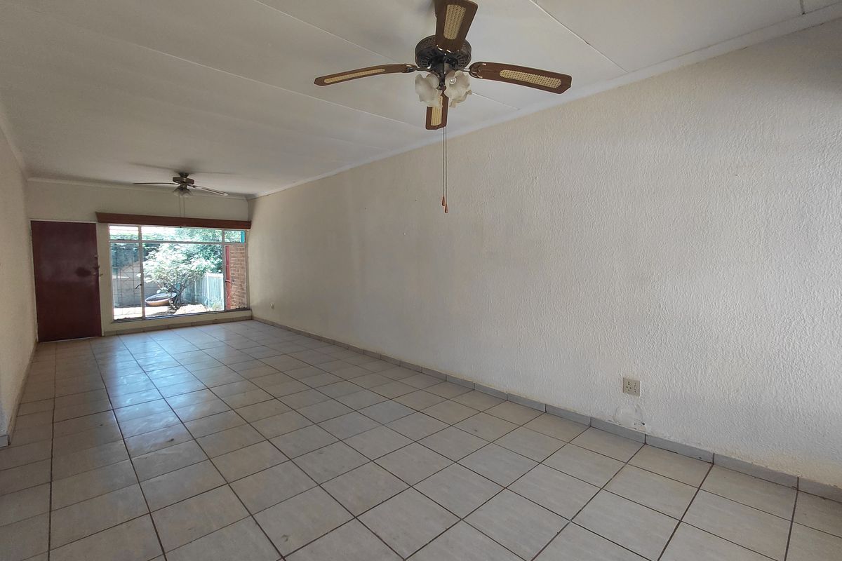 An empty, open-plan living area featuring tiled flooring, ceiling fans, and a sliding door providing access to the exterior.