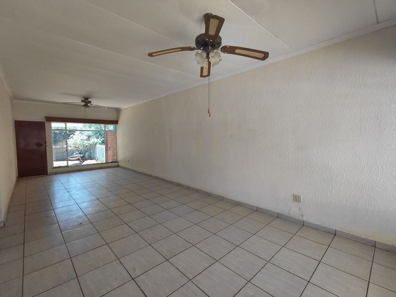 An empty, open-plan living area featuring tiled flooring, ceiling fans, and a sliding door providing access to the exterior.
