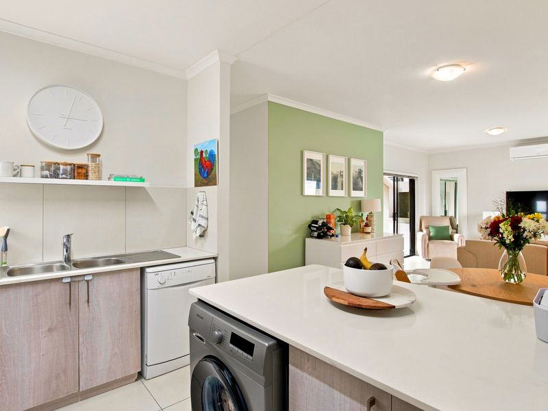 A bright open-plan living area featuring a modern kitchen with stone countertops, integrated appliances, and a seamless flow into the adjacent lounge space.