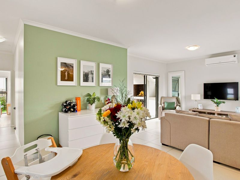 Bright open-plan living and dining area featuring neutral tiled flooring, a split-system air conditioner, and seamless access to the outdoor patio.