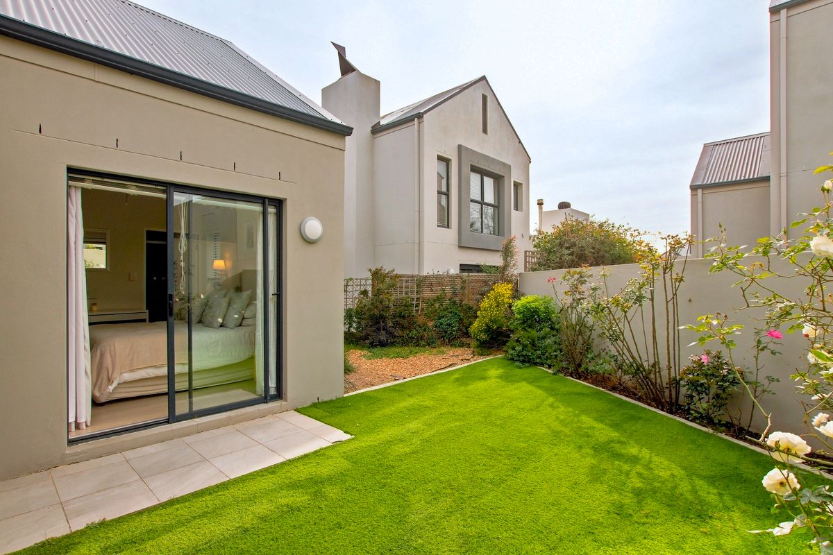 A well-maintained rear garden featuring a small tiled patio, artificial lawn, and direct access to the interior via a sliding glass door.