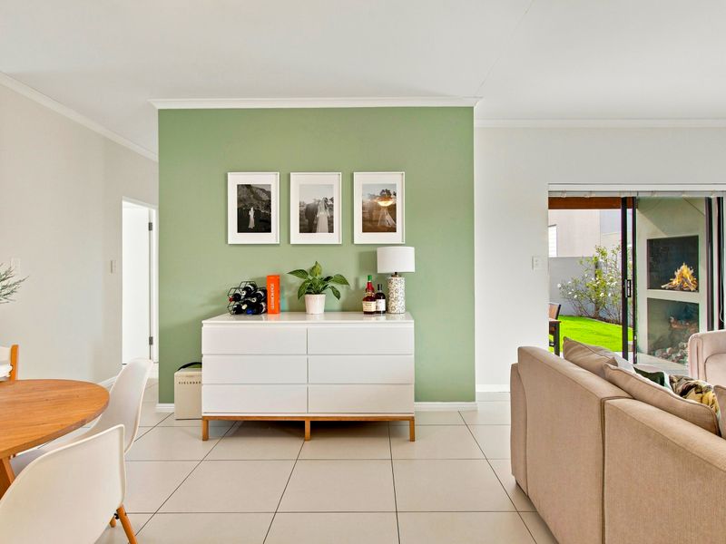 Bright open-plan living and dining area featuring neutral tiled flooring, a sage green accent wall, and seamless access to the rear garden through sliding doors.