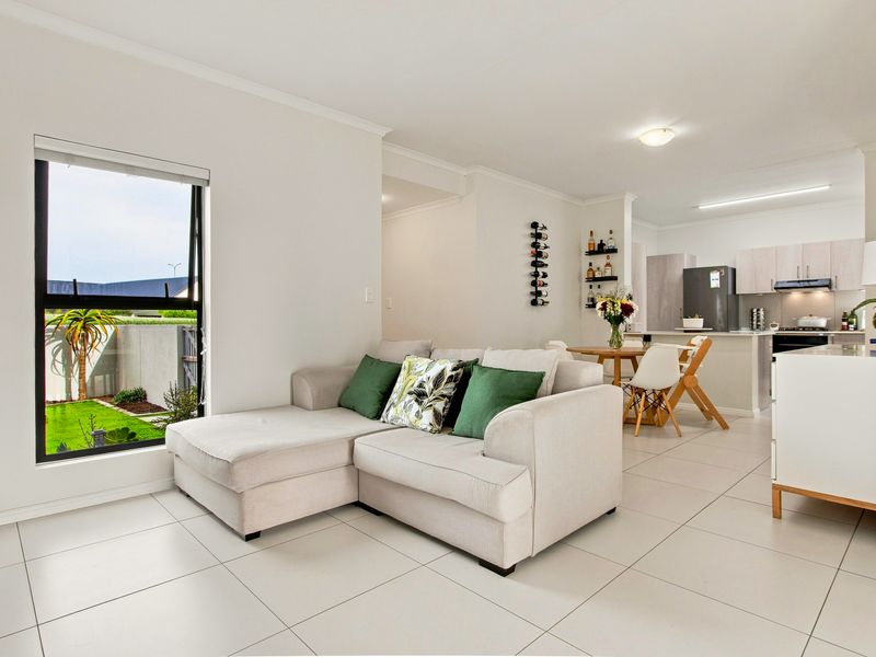 Bright open-plan living and dining area featuring modern tiled floors, neutral walls, and a functional kitchen with built-in cabinetry and appliances.